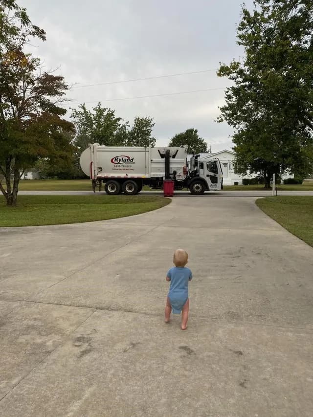 Young child watching a Ryland Environmental garbage truck from their driveway in a Georgia neighborhood